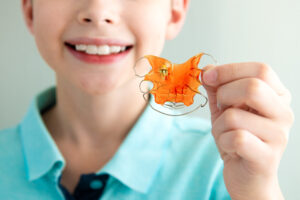 Dental plate. Expansion of the jaw in a child. A plate to heaven. There is not enough room for the molars. Happy boy holding an orthodontic plate in his hands