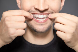 man apply whitening strip on his teeth by hands while smiling into camera