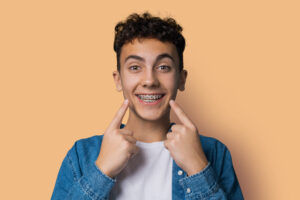 Smiling young man wearing metal braces pointing to his teeth